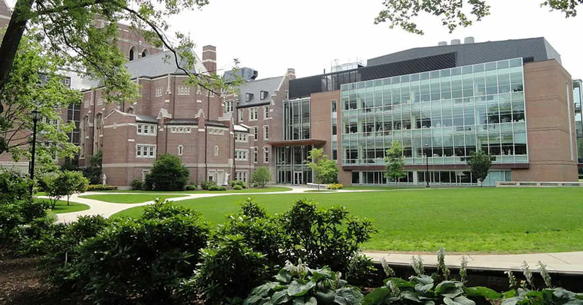 The university building at Emmanuel College, with its blend of old and modern architecture, including brick walls and large glass windows, is surrounded by a green lawn and trees. This picturesque setting is part of what makes the Emmanuel College experience so enriching according to their Common Data Set.