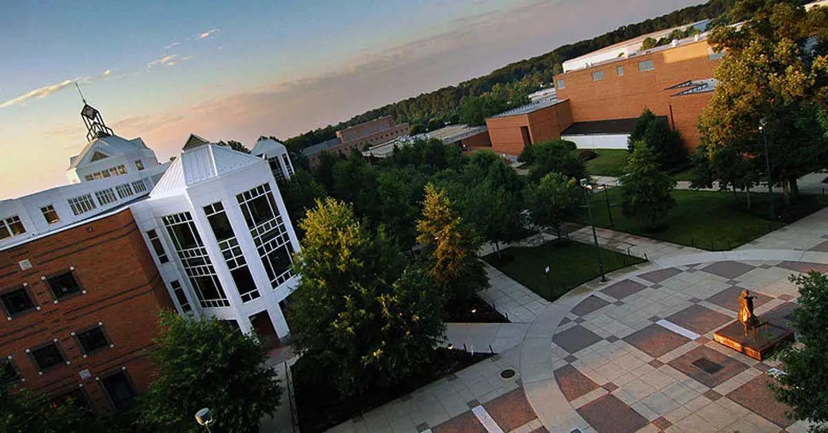 Aerial view of George Mason University campus featuring modern brick buildings, green trees, a statue, and paved walkways at sunset.