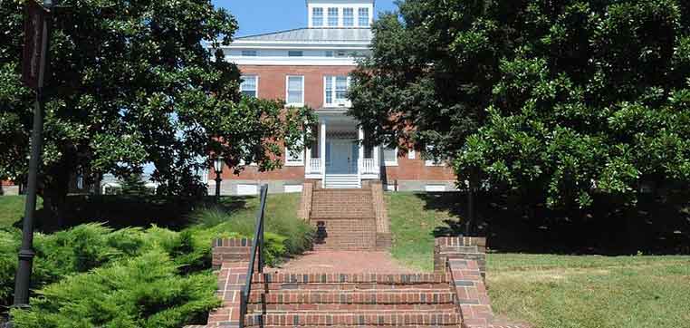 A brick building with white trim sits behind a series of brick steps, surrounded by trees and greenery, much like the scenic campus detailed in the Washington College Common Data Set.