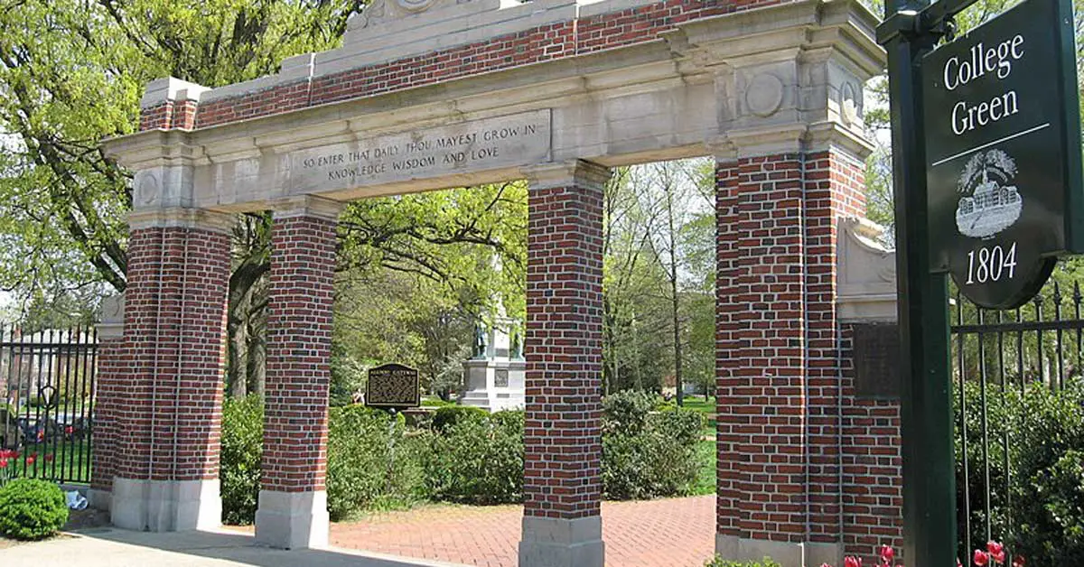 Brick and stone archway with an inscription, leading to a park-like area of trees and shrubbery. A black sign nearby reads, "College Green, 1804." This charming entrance is part of Ohio University's historic campus.