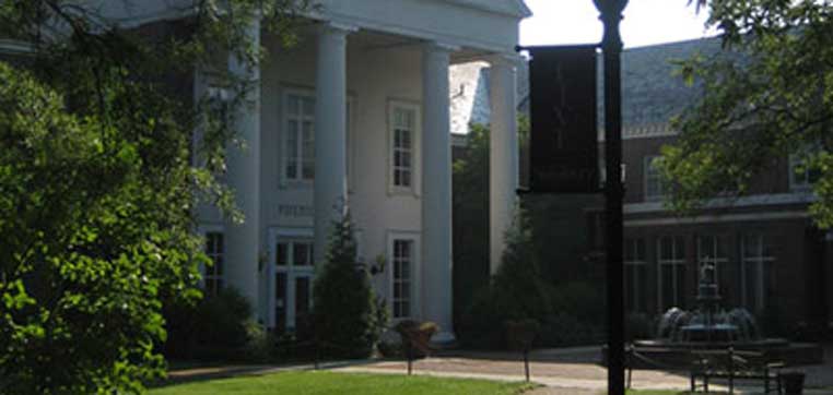 A building with large white columns at the entrance, surrounded by greenery and a lamppost. A fountain is visible on the right side, reminiscent of the classic architecture found on Salisbury University's campus.