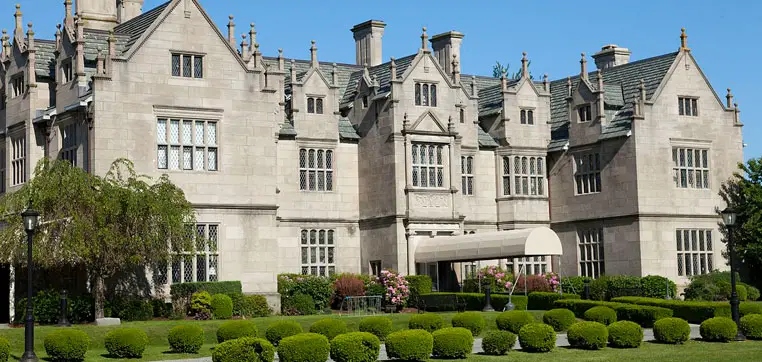 A large historic mansion with a detailed facade, multiple chimneys, and intricate architecture, surrounded by well-manicured hedges and lawns under a clear blue sky, mirrors the elegance of Salve Regina University.