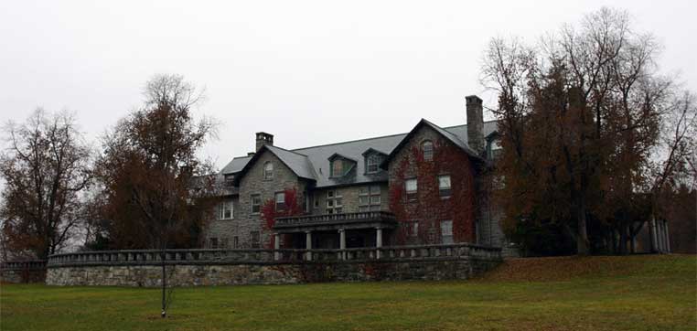 A large, old stone building with ivy-covered walls stands amid the leafless trees on a cloudy day, evoking the serene atmosphere of Bennington College in autumn.