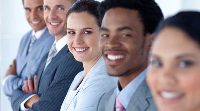 Five professionals from colleges with the most business majors, smiling in the office, dressed in business attire, standing in a staggered row.