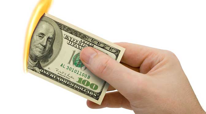 A hand holding a hundred-dollar bill being inserted into a yellow coin slot at a showcase camp.