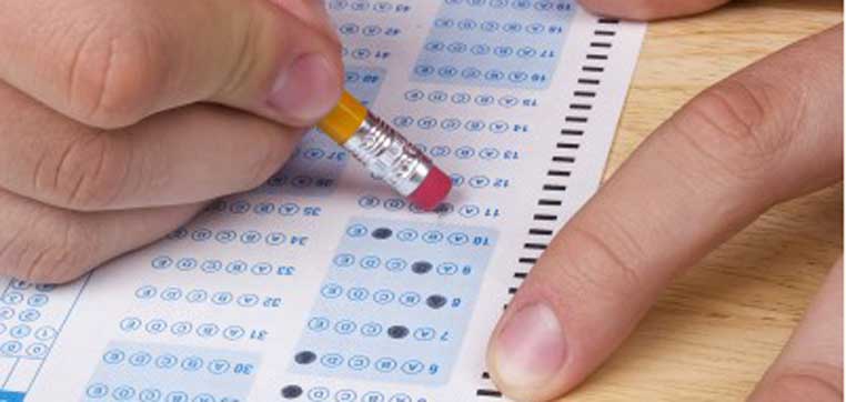 A person's hand holding a pencil eraser next to a filled bubble sheet answer sheet, with some newly erased and corrected bubbles—perfect for students navigating test-optional colleges.