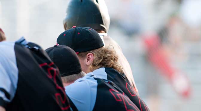 Close-up of a group of high school baseball players wearing uniforms and caps, huddled together with blurred background.